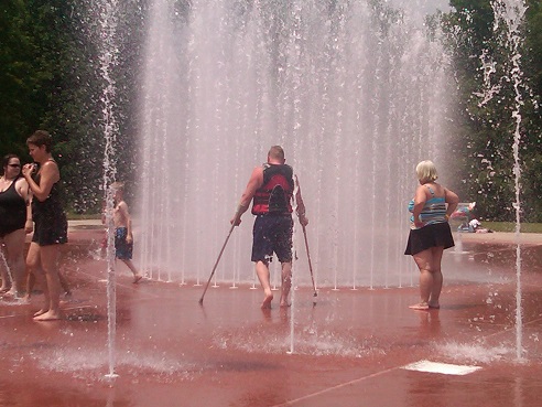man with crutches and others cool off in park fountain