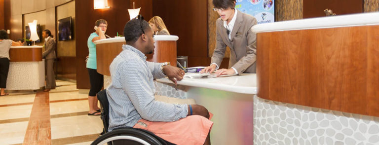 man using wheelchair checks in at accessible hotel service desk